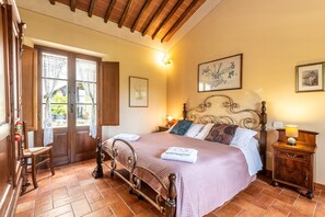 A bedroom with a wooden bed, a chair, a nightstand, and a door with curtains.