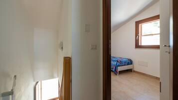 Ein Zimmer mit schrägem Dach, einem Fenster, einem Bett mit blauer Bettdecke und einer Tür.