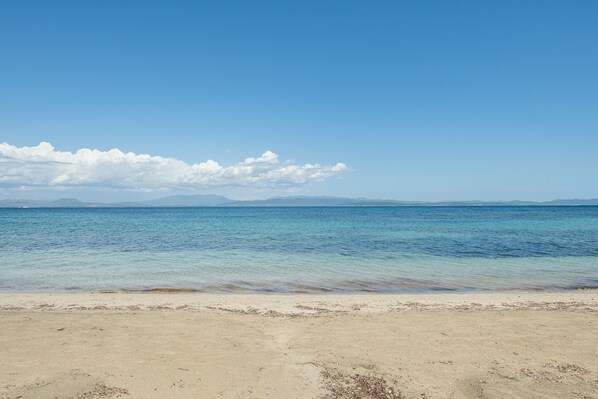 A beach with clear water, a sandy shore, and distant mountains.
