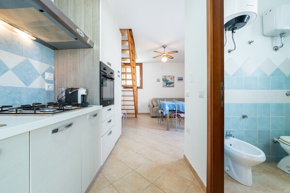 Una cucina con piano cottura a gas, forno e microonde, un'area pranzo con tavolo e sedie, e un bagno con toilette e bidet.
