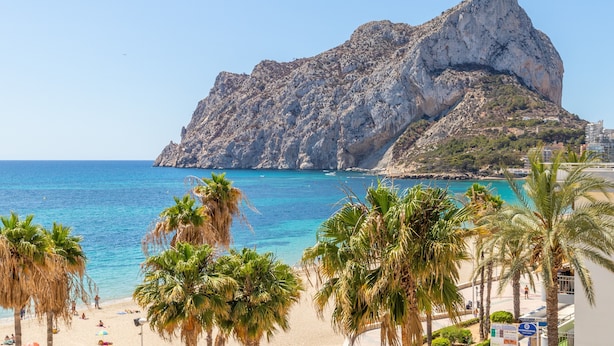 Una playa con palmeras, una montaña rocosa y un mar azul cristalino.