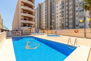A swimming pool with lounge chairs, a lifebuoy, and a high-rise building in the background. - Apartment 'Primera Linea Calpe' with Sea View, Private Pool and Air Conditioning (Calpe)