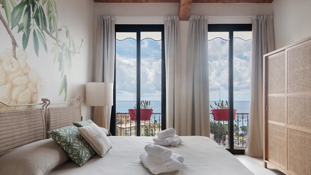 Habitación de hotel con una cama grande, vista al mar y un balcón con plantas en macetas.