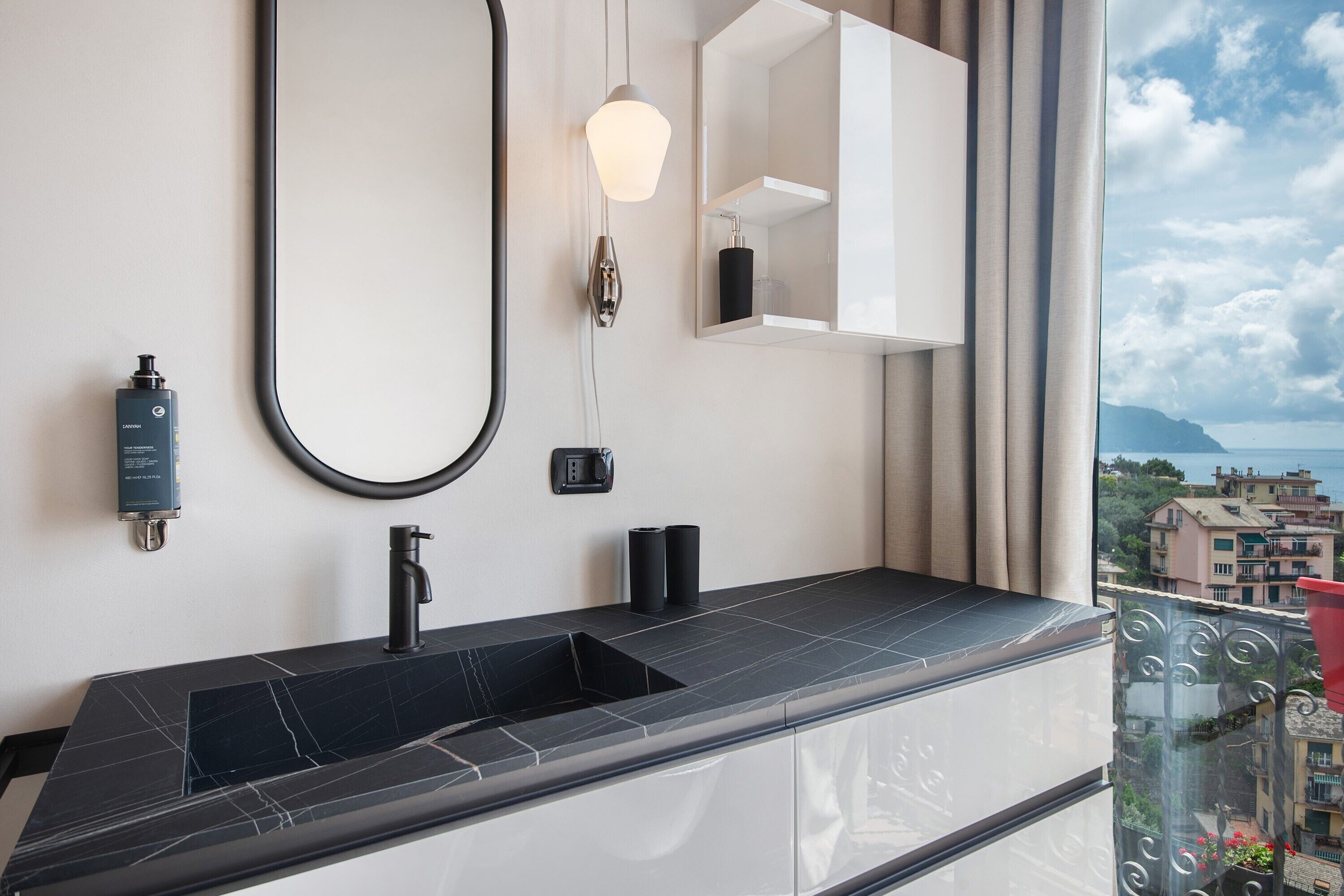 Une salle de bain avec un lavabo noir, une douchette à main, un luminaire fixé au mur et un miroir avec une étagère.