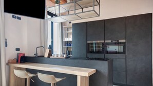 Una cocina moderna con barra de madera, dos taburetes y electrodomésticos integrados.
