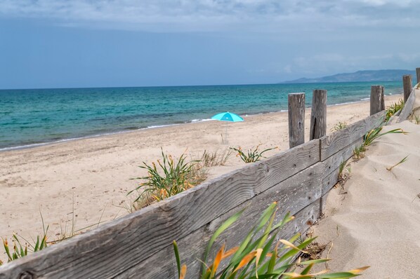 Une plage avec une clôture en bois, un parasol bleu et une vue sur l’océan.