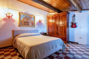A bedroom with a bed, a wooden wardrobe, a guitar, and a painting on the wall. - Apartment 'La Contessa' with Mountain View, Wi-Fi and Air Conditioning (Sennori)