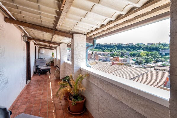 A balcony with a view of a cityscape, a potted plant, and a chair.