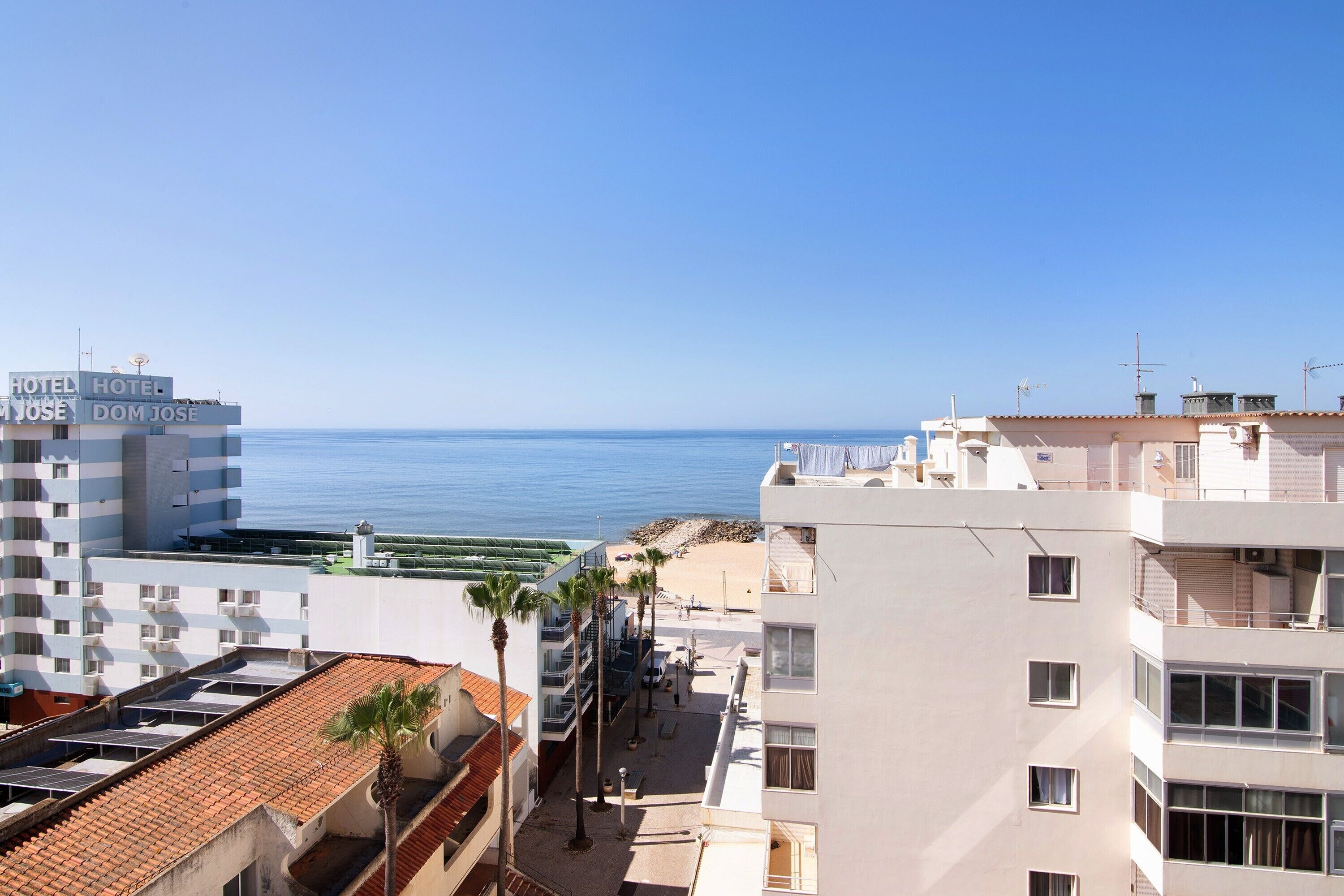 A hotel with multiple floors, a beach view, and a clear sky.