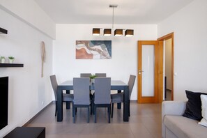 A dining area with a table and chairs, a painting on the wall, a ceiling light fixture, and a wooden door.
