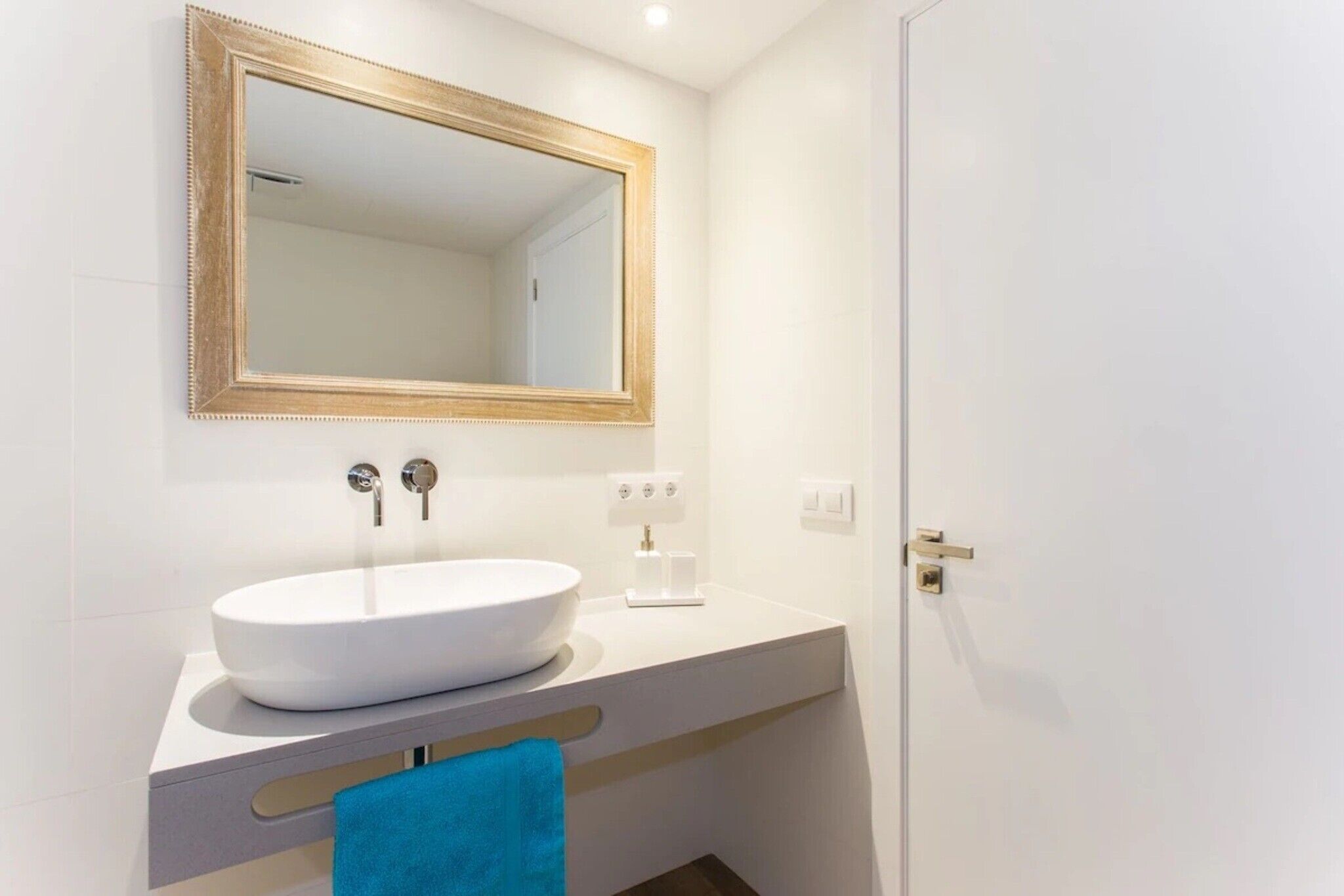 A bathroom with a white sink, a gold-framed mirror, and a blue towel.