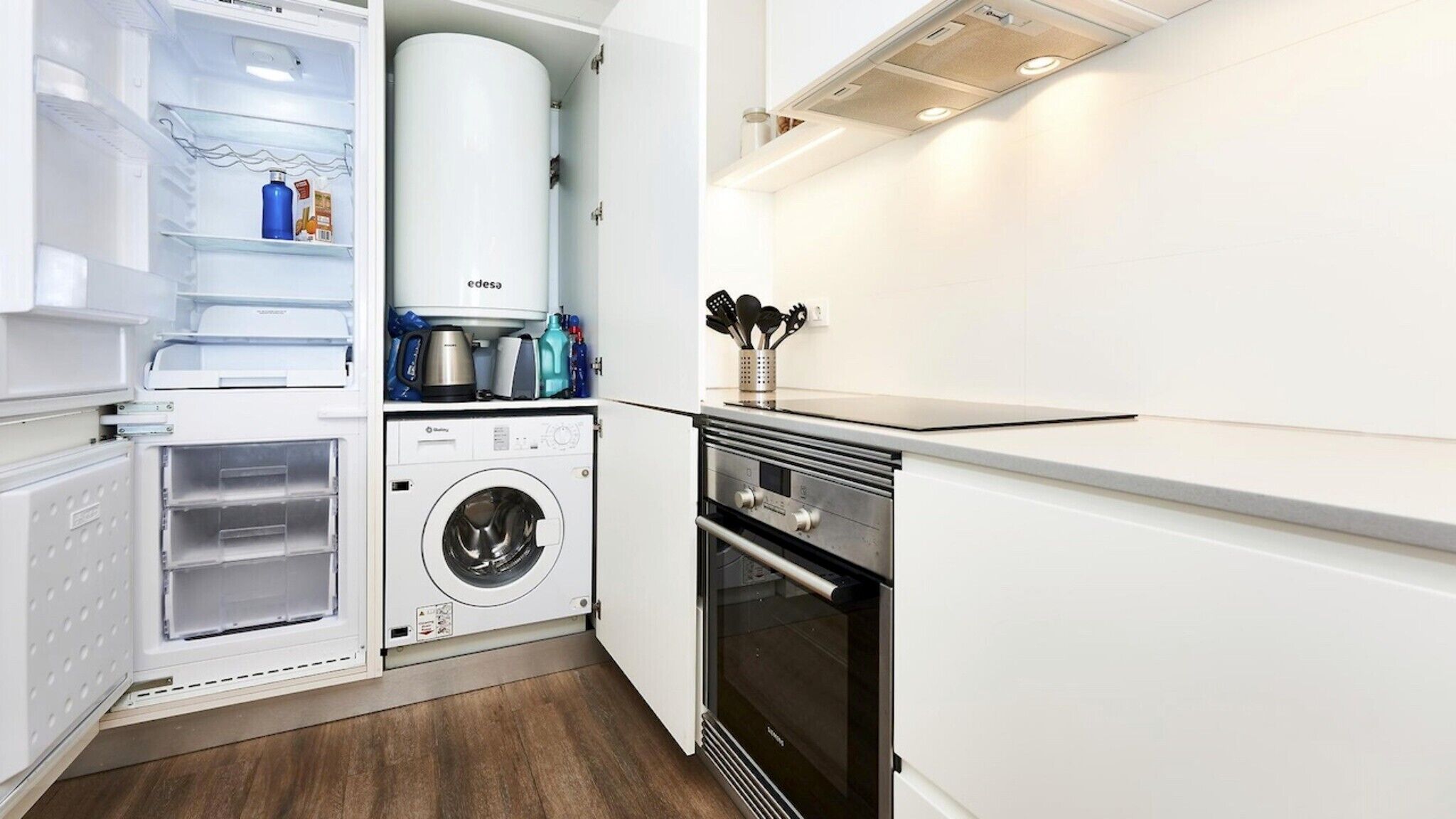 Una cocina compacta equipada con lavadora integrada, horno y refrigerador con dispensador de agua.