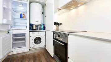 Una cocina compacta equipada con lavadora integrada, horno y refrigerador con dispensador de agua.