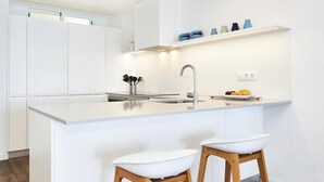 Cocina moderna con encimera blanca, pileta de acero inoxidable y taburetes de bar.