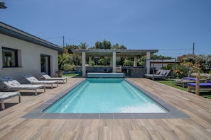 Een rechthoekig zwembad met een pergola en ligbedden.