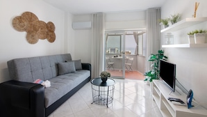 A modern living room with a grey sofa, a round black coffee table, a flat-screen TV, and a white entertainment unit. - 'T1 with Sea View' Apartment with Wi-Fi and Air Conditioning (Quarteira)