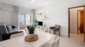 A modern living room with a sofa, dining table, TV, and a small plant. - 'T1 with Sea View' Apartment with Wi-Fi and Air Conditioning (Quarteira)