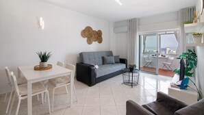 A modern living room with a sofa, dining table, chairs, and a balcony with a view. - 'T1 with Sea View' Apartment with Wi-Fi and Air Conditioning (Quarteira)
