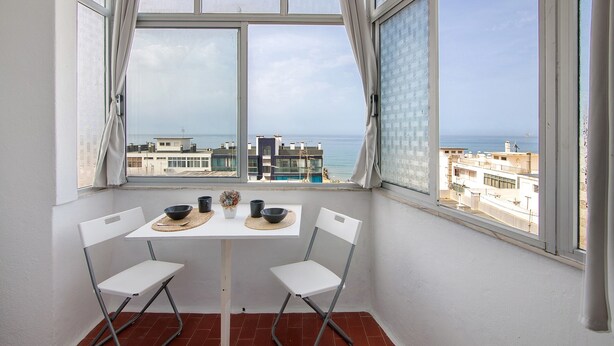 A balcony with a table and chairs, a view of the sea, and buildings in the background. - 'T1 with Sea View' Apartment with Wi-Fi and Air Conditioning (Quarteira)