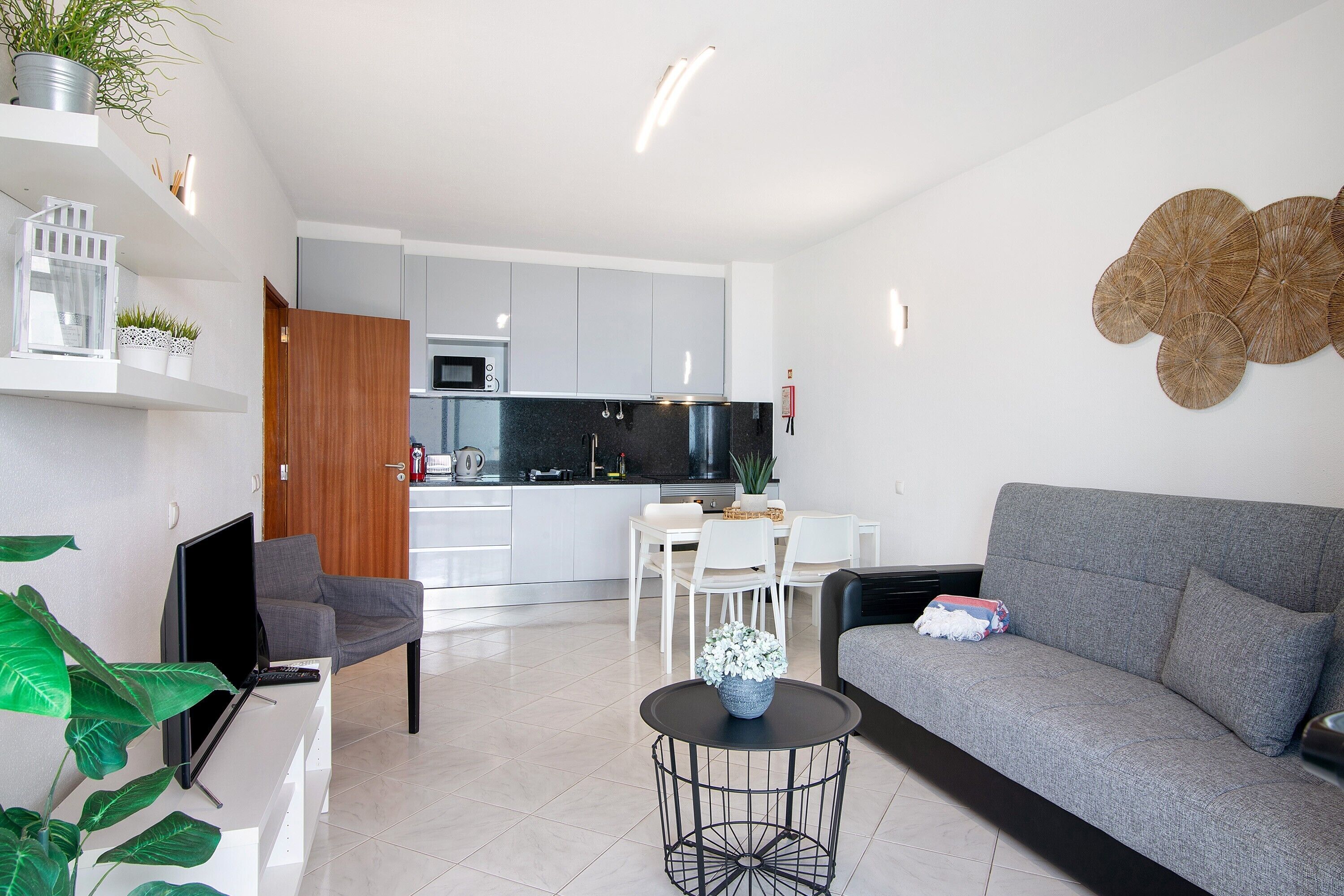 Ein modernes Wohnzimmer mit einem grauen Sofa, einem runden schwarzen Couchtisch und einem Fernseher auf einem weißen Schrank.