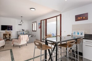 A modern kitchen with a dining area, a sofa, and a TV.