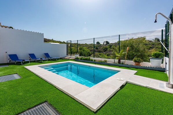 A rectangular pool with blue water, surrounded by artificial green grass, and three blue lounge chairs.