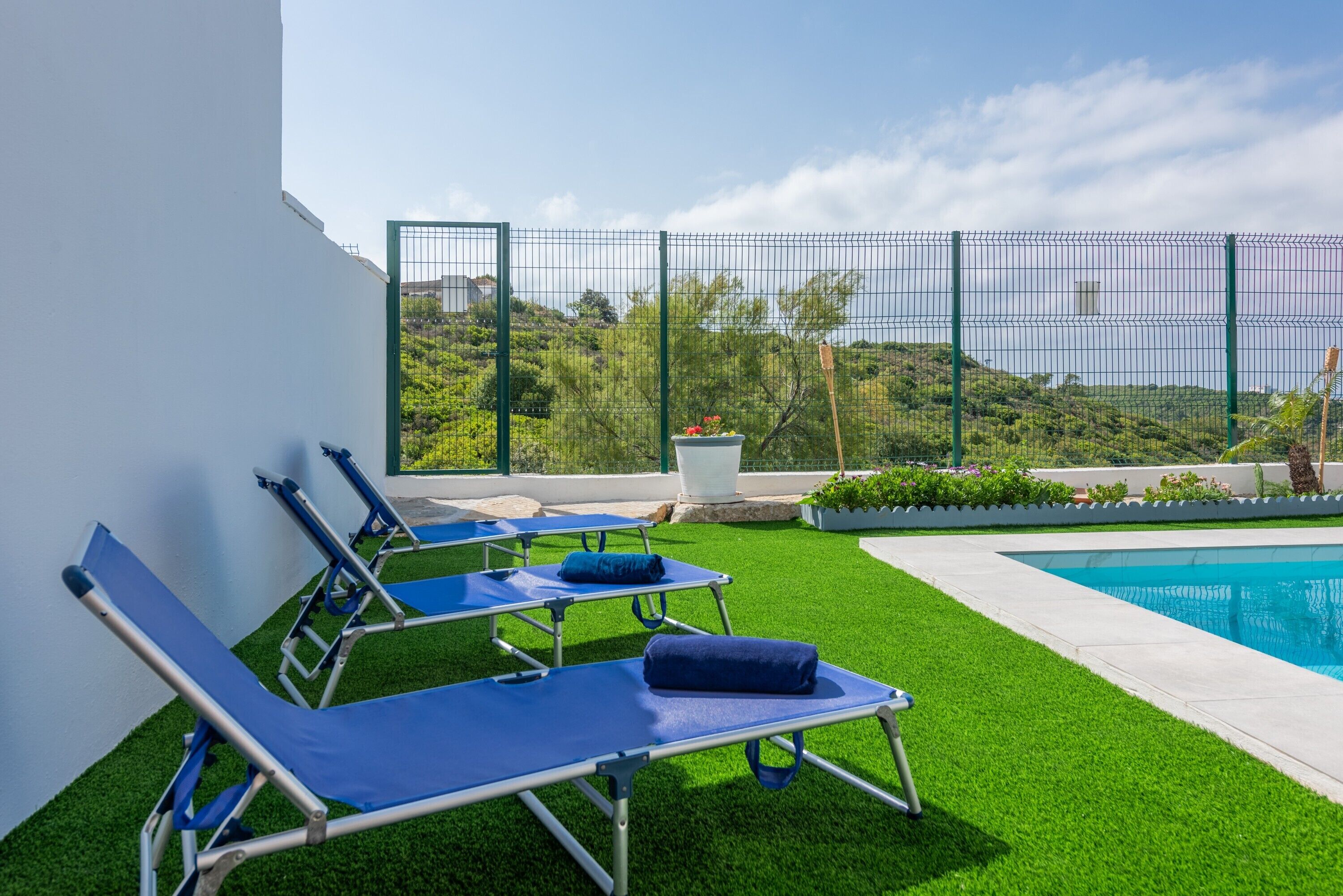 Zona junto a la piscina con sillones reclinables, piscina y vistas a zonas verdes y colinas.
