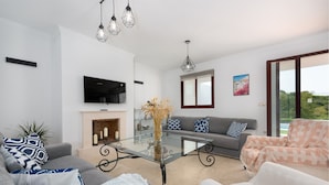 Een moderne woonkamer met een glazen salontafel, grijze banken en een open haard.