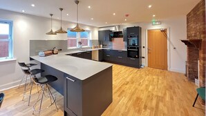A modern kitchen with a large island, bar stools, and built-in appliances. - Transvaal House Ely  (Ely)