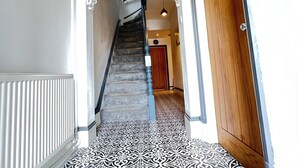 A hallway with patterned floor tiles, a wooden door, and a staircase with a blue handrail. - Transvaal House Ely  (Ely)