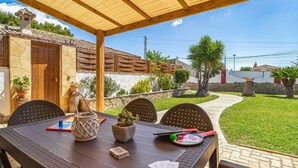 Eine Terrasse im Freien mit einem Holztisch, Stühlen und einer Pergola darüber.