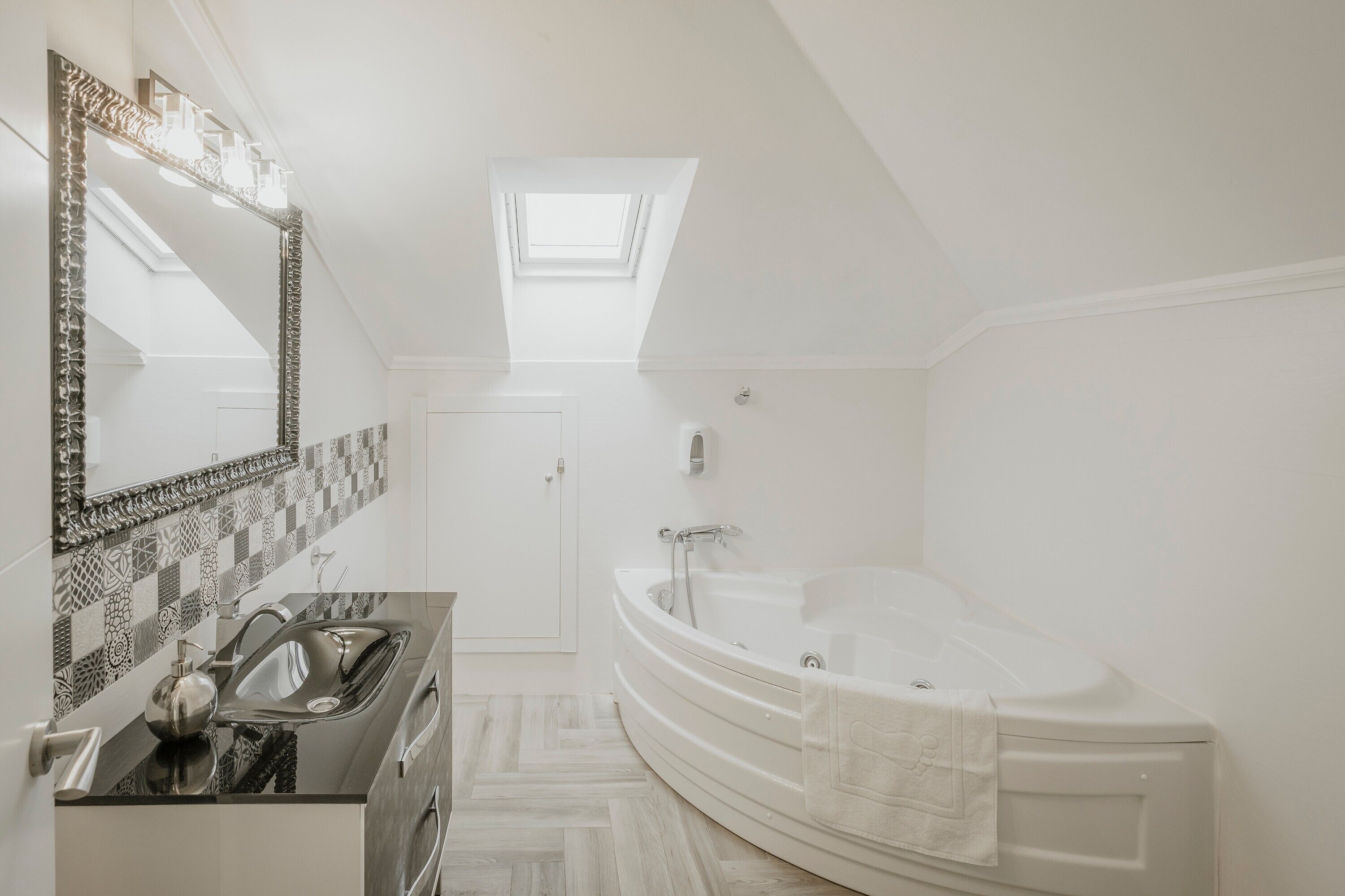 Une salle de bain moderne avec une baignoire sur pieds, un grand miroir et une lucarne.