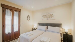 A bedroom with two beds, a nightstand with a lamp, a wooden wardrobe, and a wall-mounted artwork. - Torres 1 in Valdivielso Valley, Mountain Views & Garden (MERINDAD DE VALDIVIELSO)