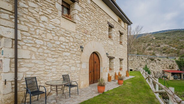A stone building with a wooden door, outdoor seating, and a grassy area. - Torres 1 in Valdivielso Valley, Mountain Views & Garden (MERINDAD DE VALDIVIELSO)