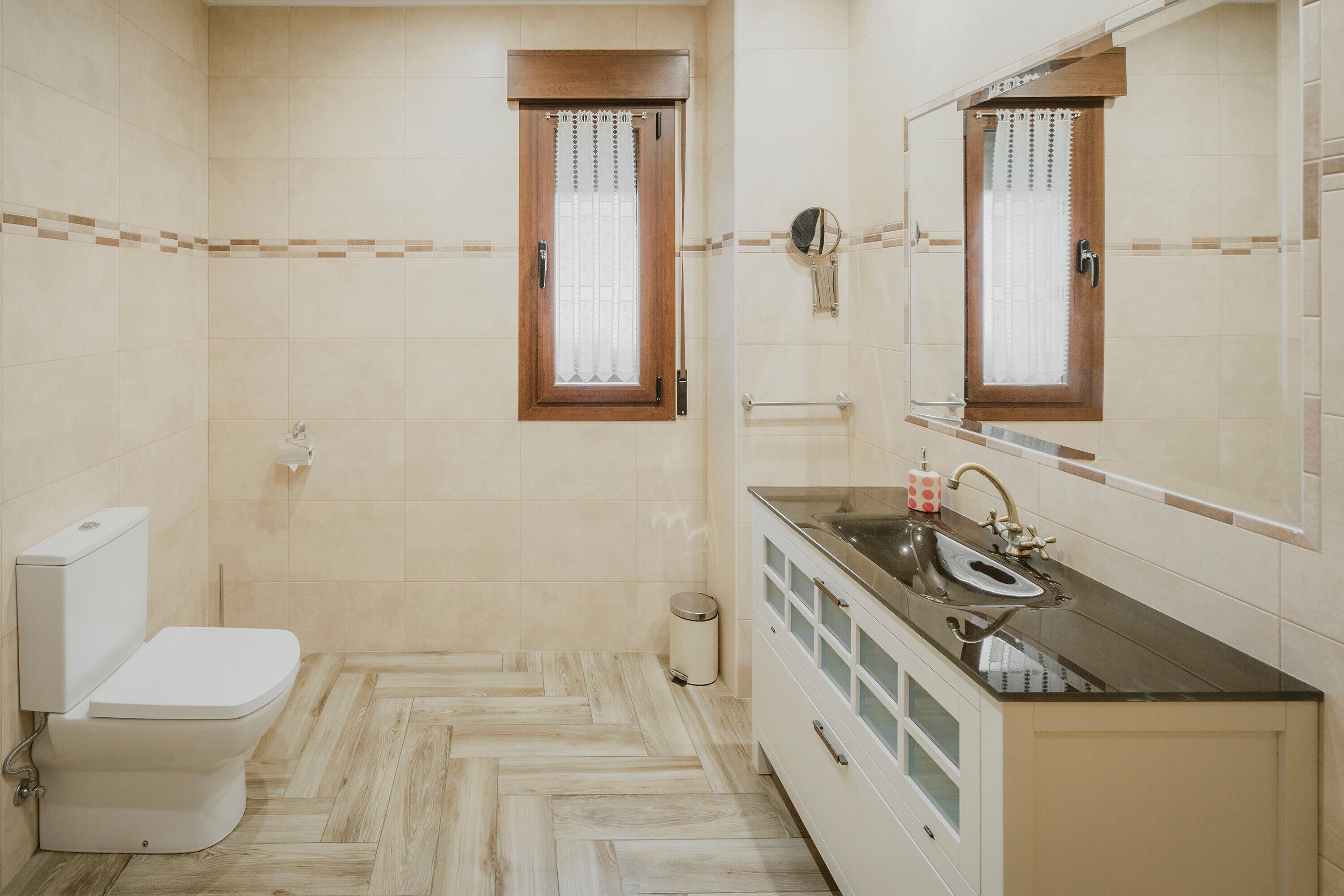 Un baño con inodoro, lavamanos, espejo y paredes con azulejos.