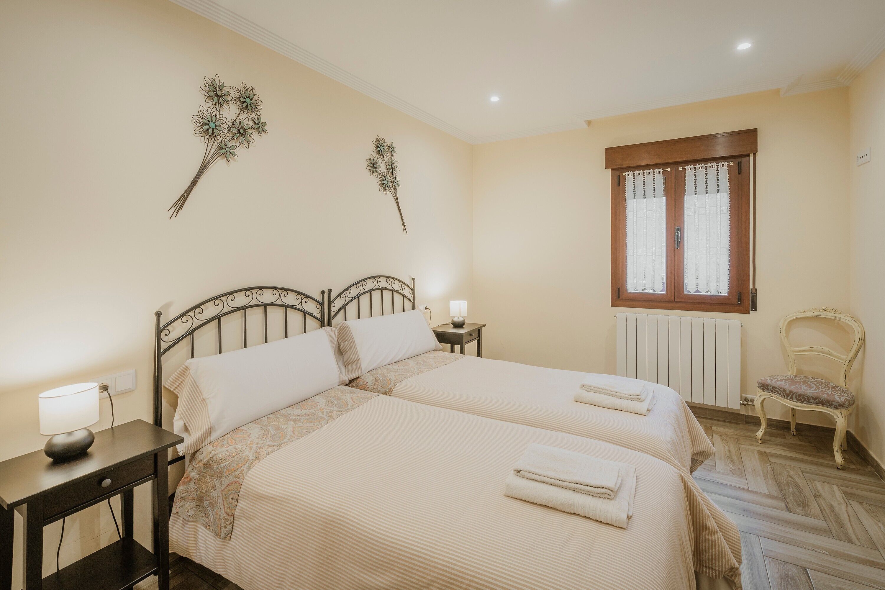 A double bed with a nightstand, a chair, a window with curtains, and wall decorations.