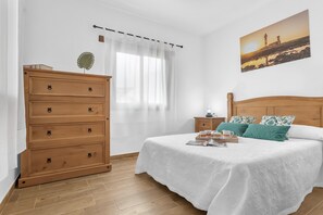 Ein Schlafzimmer mit einem hölzernen Schminktisch, einem Bett mit weißer Bettwäsche, einem Nachttisch, einer Lampe und einem Gemälde eines Leuchtturms an der Wand.