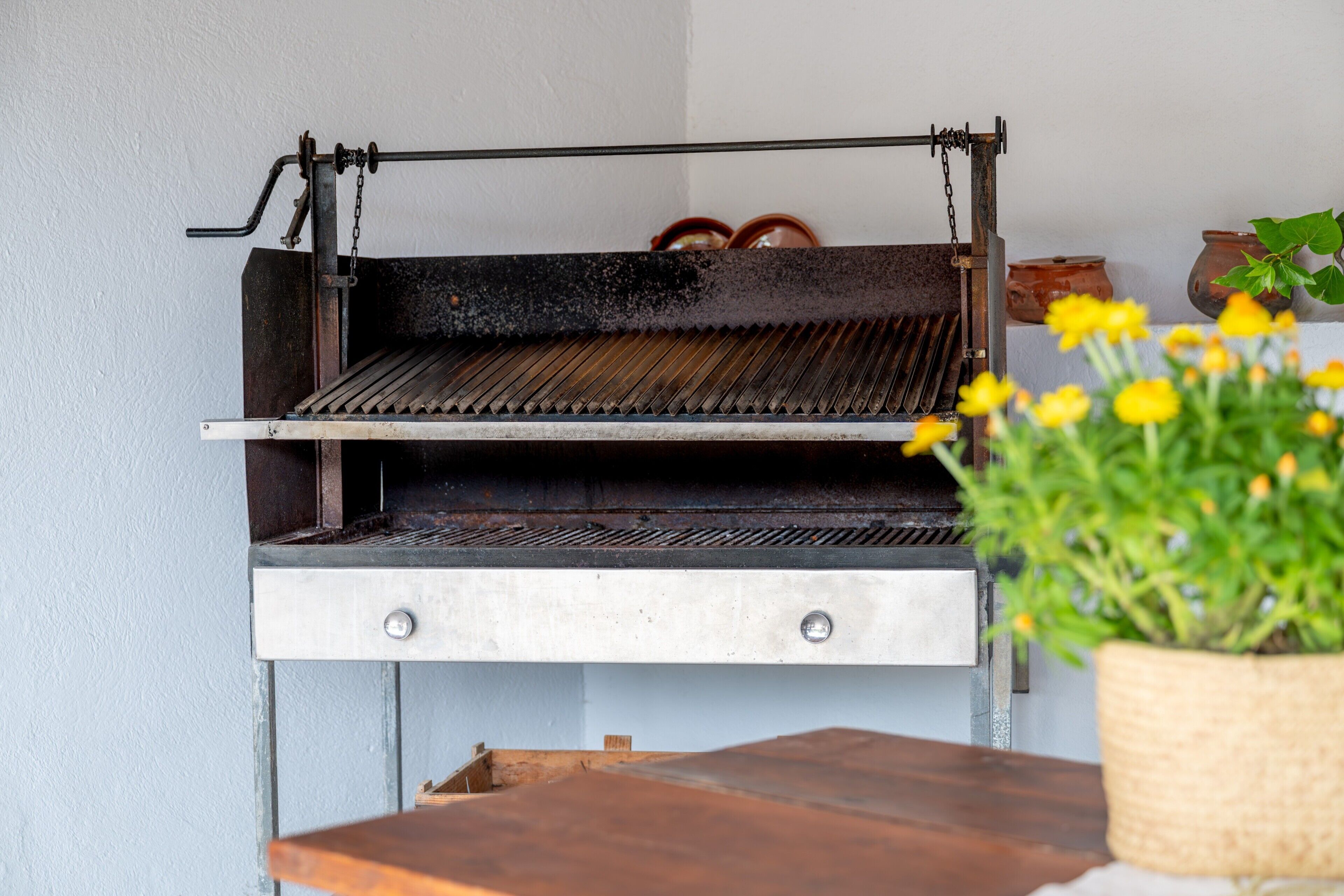 A grill with a metal grate, a wooden table, and a potted plant with yellow flowers.