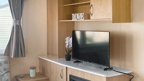 A compact room with a flat-screen TV on a white shelf, a small potted orchid, and a 'LOVE' sign above the TV. - 3 bedroom accommodation in Heysham, near Lancaster (Heysham, near Lancaster)