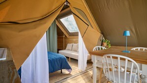 Une tente équipée d’un lit, d’une table, de chaises et d’une lampe.