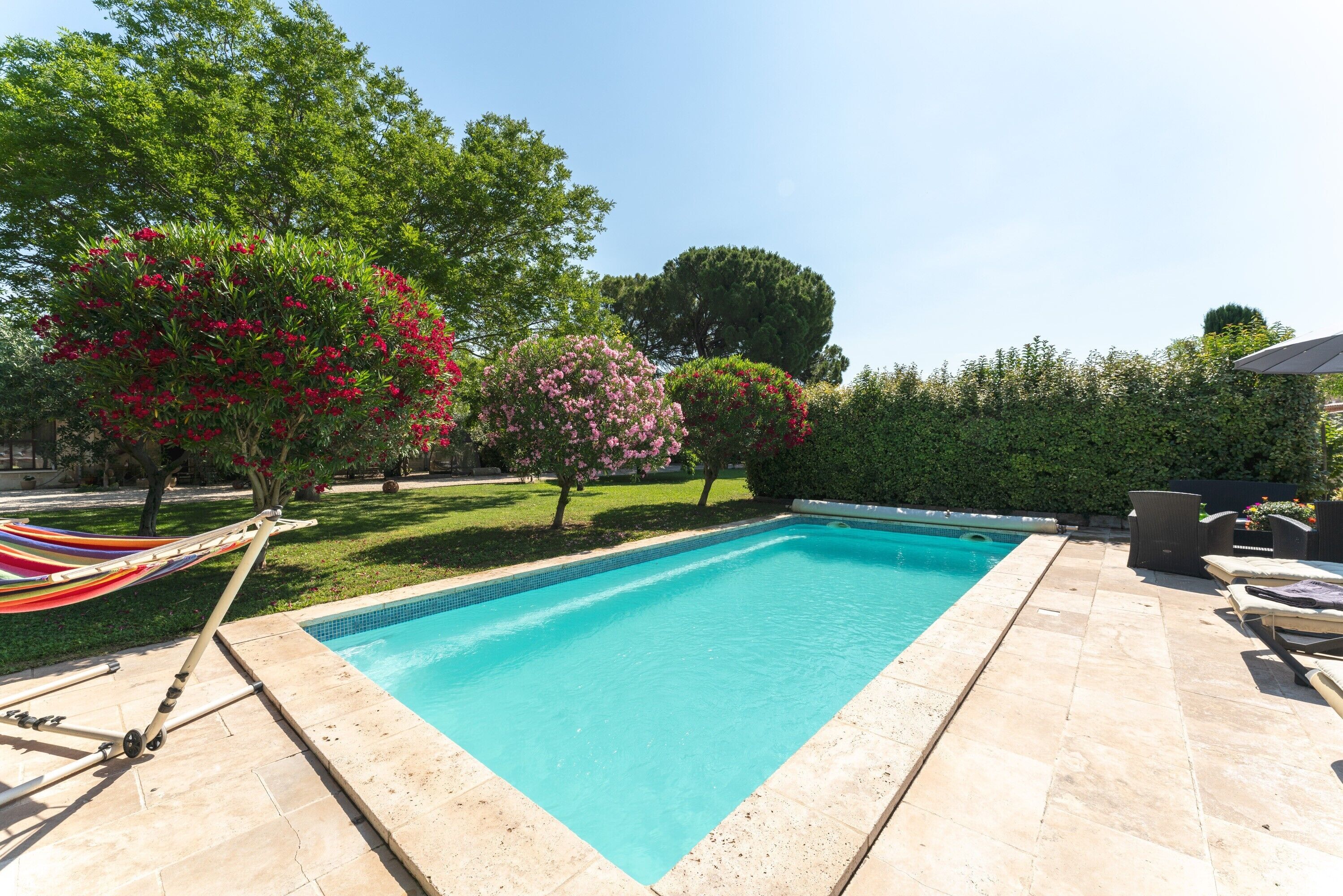 Une piscine rectangulaire dont les bords sont recouverts de carreaux, entourée d’un espace patio aménagé avec des chaises longues et un hamac.