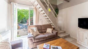 A living room with a brown leather sofa, a wooden coffee table, a television, and a staircase leading to an upper level. - Country House 'Le Mas' with Shared Pool, Wi-Fi, and Air Conditioning (Graveson)