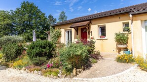 A house with a red door, a garden with various plants and flowers, and a clear blue sky. - The Calm of Périgord Noir – Comfortable House near Sarlat-la-Canéda (Carsac-Aillac)