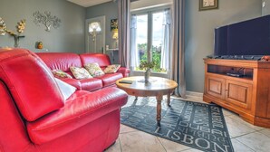 A living room with a red leather sofa, a round wooden coffee table, and a large flat-screen TV on a wooden cabinet. - The Calm of Périgord Noir – Comfortable House near Sarlat-la-Canéda (Carsac-Aillac)