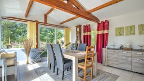 A dining area with a wooden table, chairs, and a kitchen with cabinets and a clock. - The Calm of Périgord Noir – Comfortable House near Sarlat-la-Canéda (Carsac-Aillac)