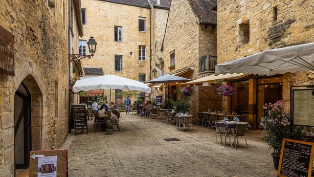 A cobblestone street with outdoor seating, stone buildings, and a sign for a restaurant. - The Calm of Périgord Noir – Comfortable House near Sarlat-la-Canéda (Carsac-Aillac)