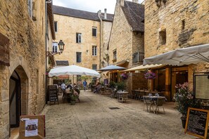 Une rue pavée avec des tables en terrasse, des bâtiments en pierre et une enseigne indiquant un restaurant.