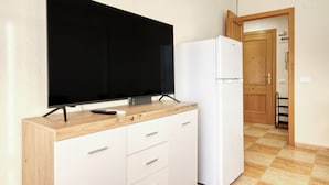 A kitchenette with a flat-screen TV, a white refrigerator, and wooden cabinetry.