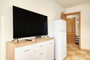 Une petite cuisine équipée d’un téléviseur à écran plat, d’un réfrigérateur blanc et de meubles de rangement en bois.