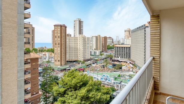 A high-rise building with multiple floors, a balcony, and a view of a cityscape with various buildings and a park area.